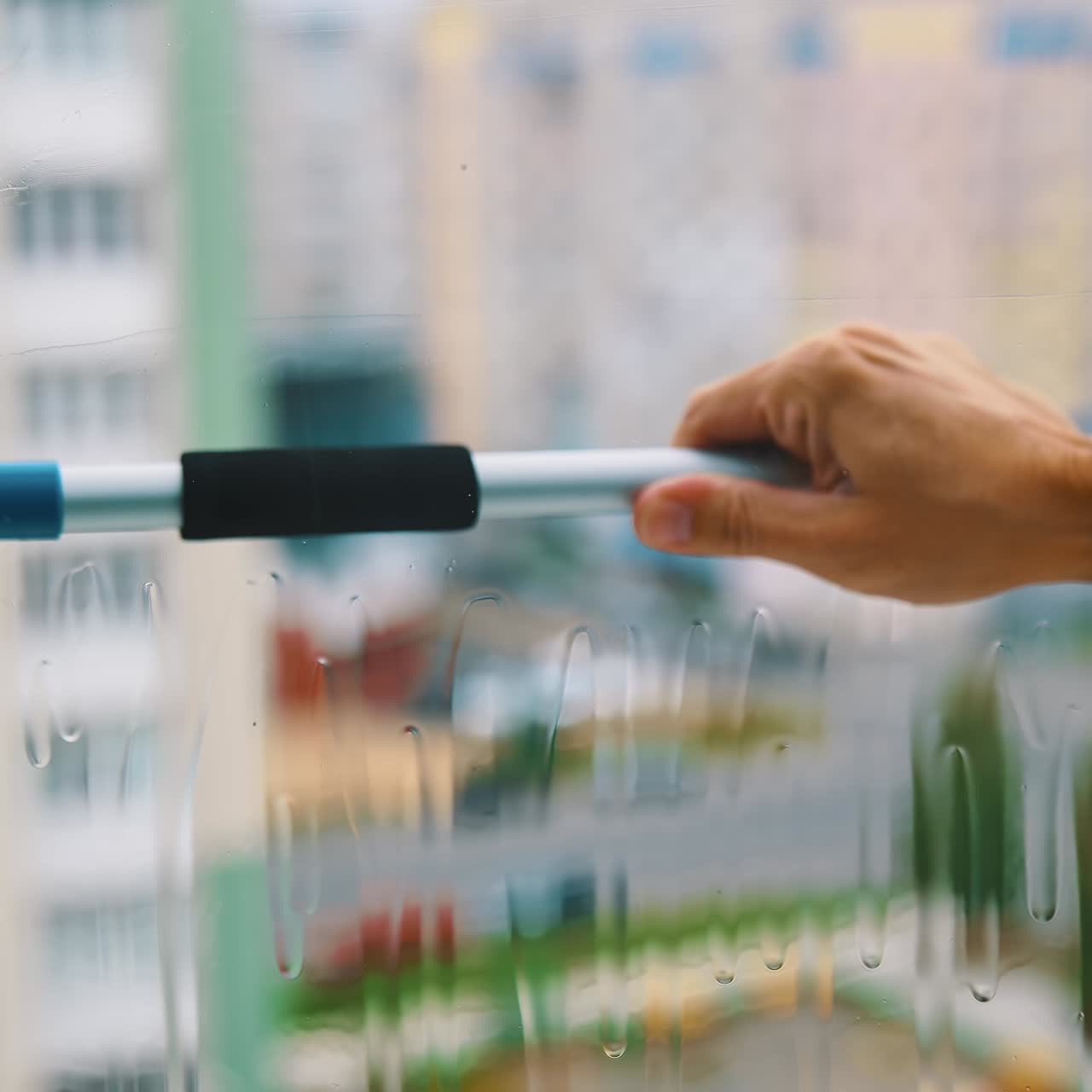 Man's hand with special brush cleaning window. Worker is washing dirty window glass with a liquid and wiping it in a flat of multi-storey building