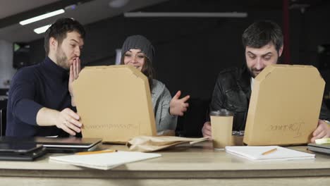 team of young creative workers opening paper boxes with pizza being surprised and happy. pizza delivery to office. slow motion