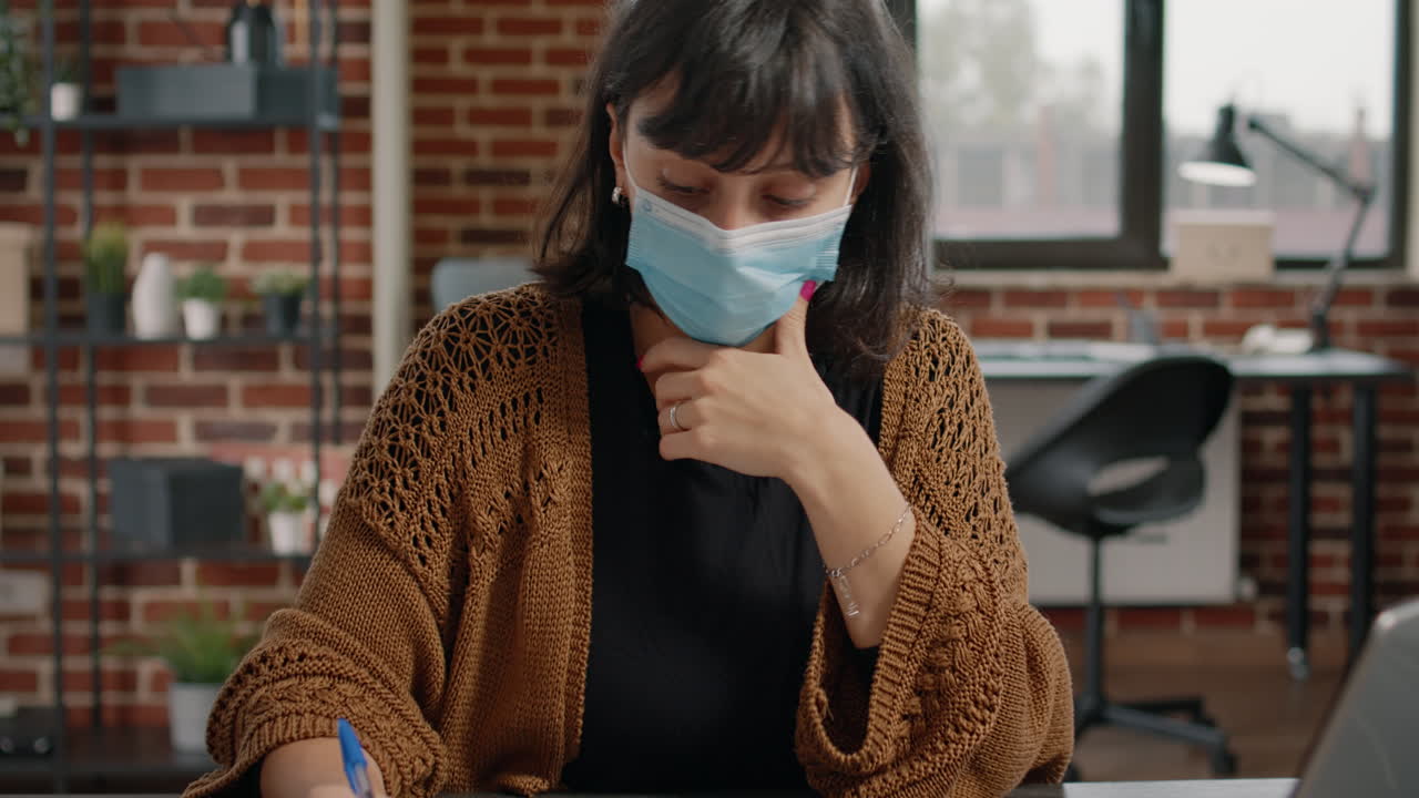 Donna che indossa una mascherina che lavora alla scrivania in ufficio
