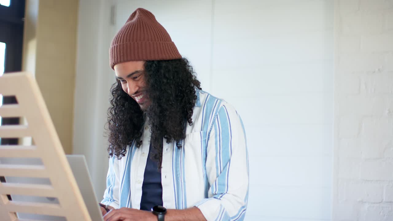 Homem de gorro cumprimentando um amigo com um high-five antes de digitar no laptop em uma mesa alta para trabalhar