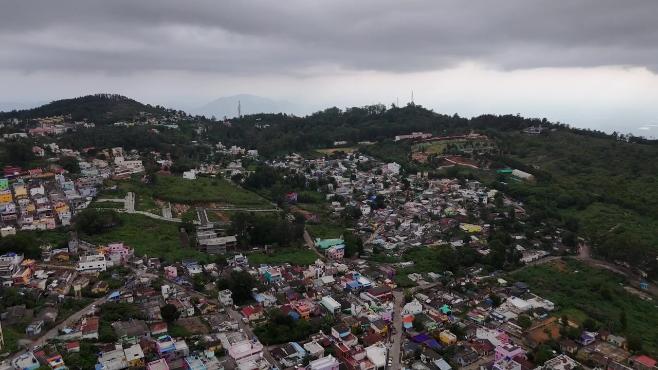 Ripresa con drone che cattura Yercaud con colline ondulate, lussureggianti piantagioni di caffè, case colorate sulle colline, valli boscose e un cielo coperto. La ripresa aerea cinematografica evidenzia il clima fresco e il paesaggio suggestivo