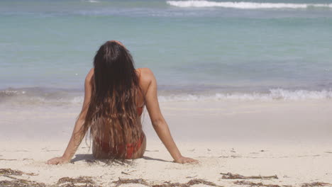 Blick-Hinter-Ein-Latino-Mädchen,-Das-Am-Weißen-Sandstrand-Sitzt-Und-Die-Ruhe-Der-Meereswellen-Genießt