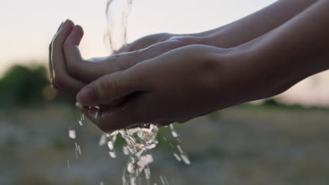 mujer de cerca lavando las manos bajo el grifo con agua dulce en tierras de cultivo rurales al amanecer