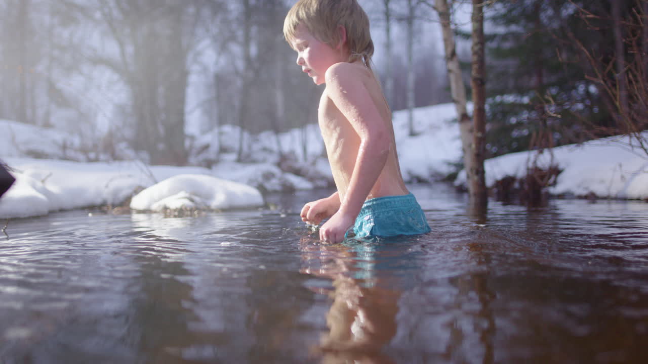 Young Scandinavian boy plunges into cold river through snowy woods after sauna