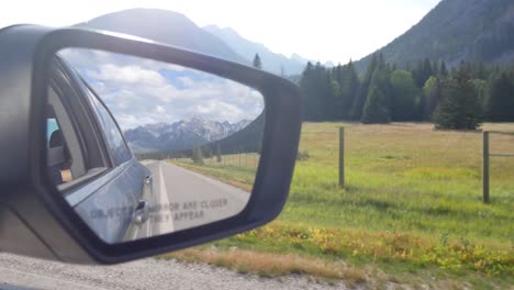 vista panorámica del camión del espejo lateral mientras se mueve con la vista reflejada de la carretera y los alrededores con un bosque de pinos verdes y montañas rocosas en alberta, canadá