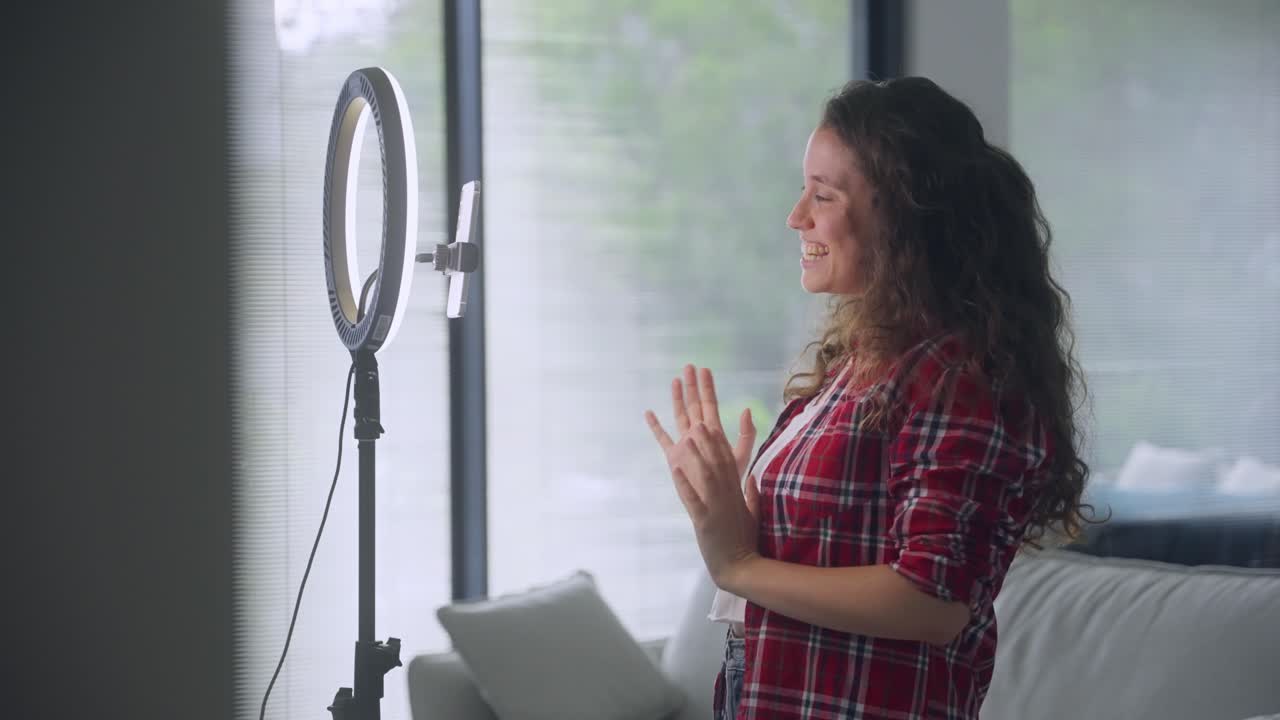 Tired or nervous stressed influencer or social media content creator filming herself with smartphone and light ring stand at home or apartment. Getting ready for live streaming to online followers