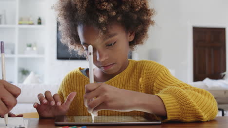 Pre-teen-African-American-schoolgirl-sitting-at-table-using-tablet-computer,-close-up
