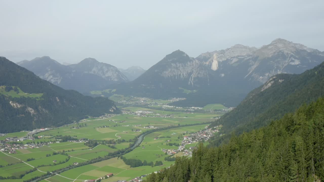 Wide-angle aerial view of a green alpine valley with a river flowing through quaint Austrian villages.