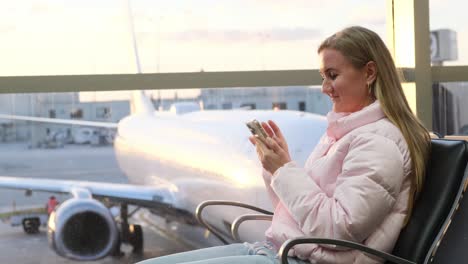 a relaxed traveler uses her phone while sitting by the window, waiting to board her flight