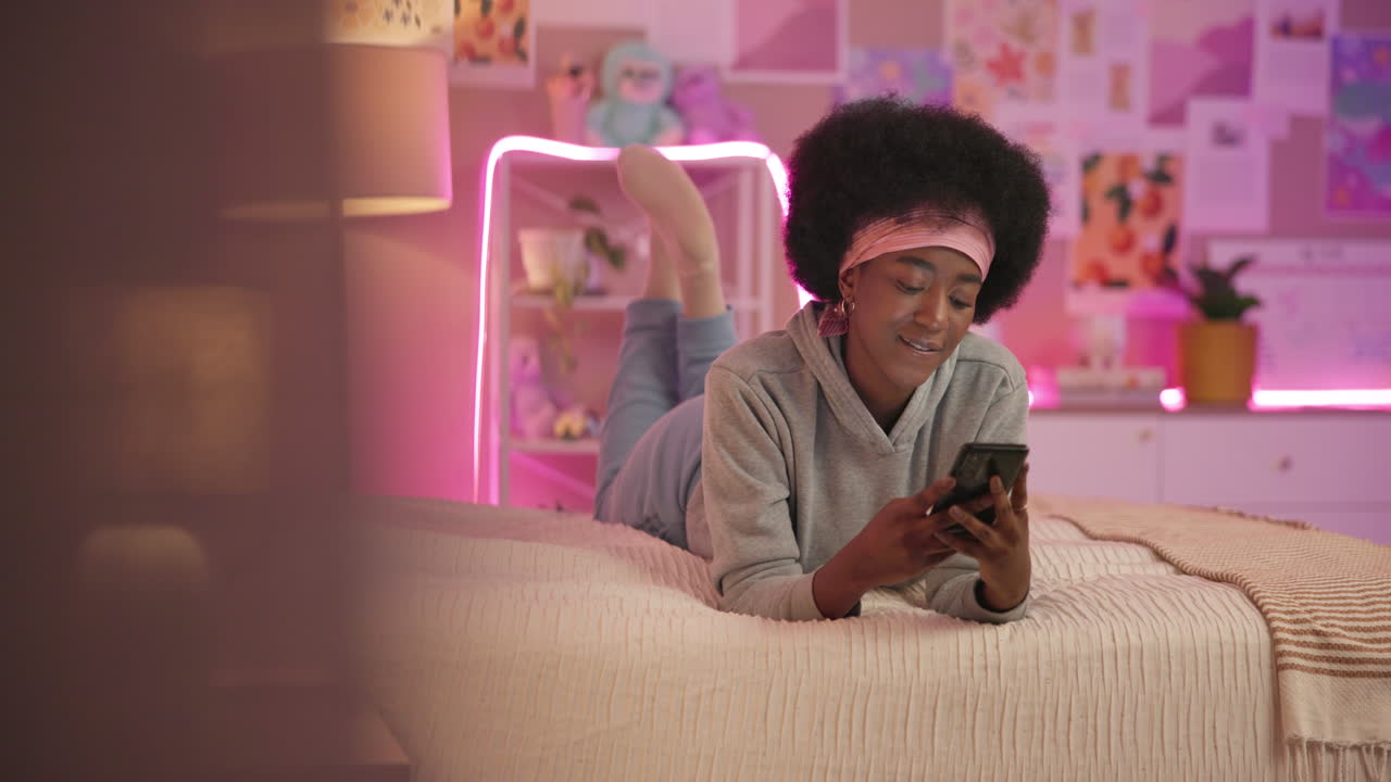 una mujer joven está acostada en una cama usando su teléfono, y sonriendo.