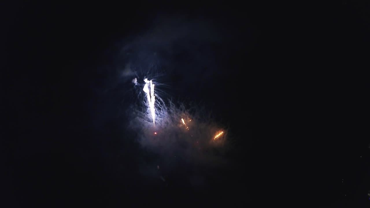Aerial flight over a fireworks display during summer time at the 4th of July, with multiple different color fireworks displays from a unique, high elevation perspective.