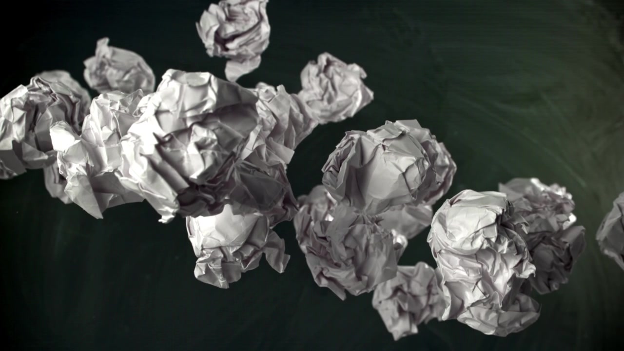 Palline di carta accartocciate che fluttuano verso l'alto contro una lavagna scura