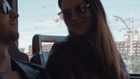 una pareja con gafas de sol sentada en un autobús en movimiento y hablando