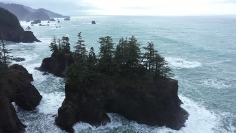 Excelente-Toma-Aérea-De-Pinos-En-Una-Gran-Roca-Frente-A-La-Costa-De-Oregon-En-Un-Día-Nublado