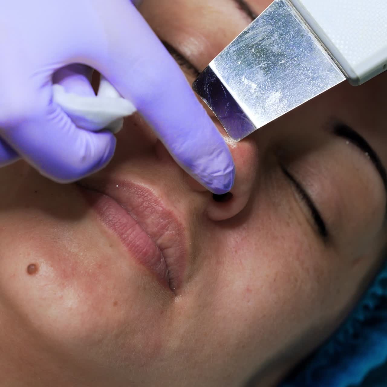 Caucasian woman undergoing skincare procedures. Beauty master uses ultrasonic scrubber for cleansing nose skin pores. Extreme close up