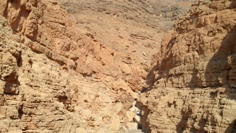 Bird's-eye-view-from-drone-going-through-rocky-valleys-in-desert-mountains,-United-Arab-Emirates