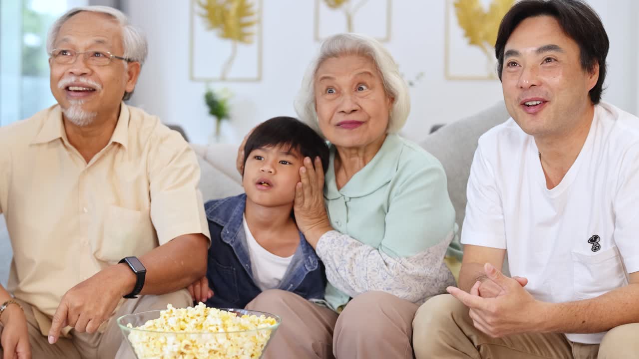 A joyful Asian family watches a movie, sharing laughter and popcorn in a cozy living room setting