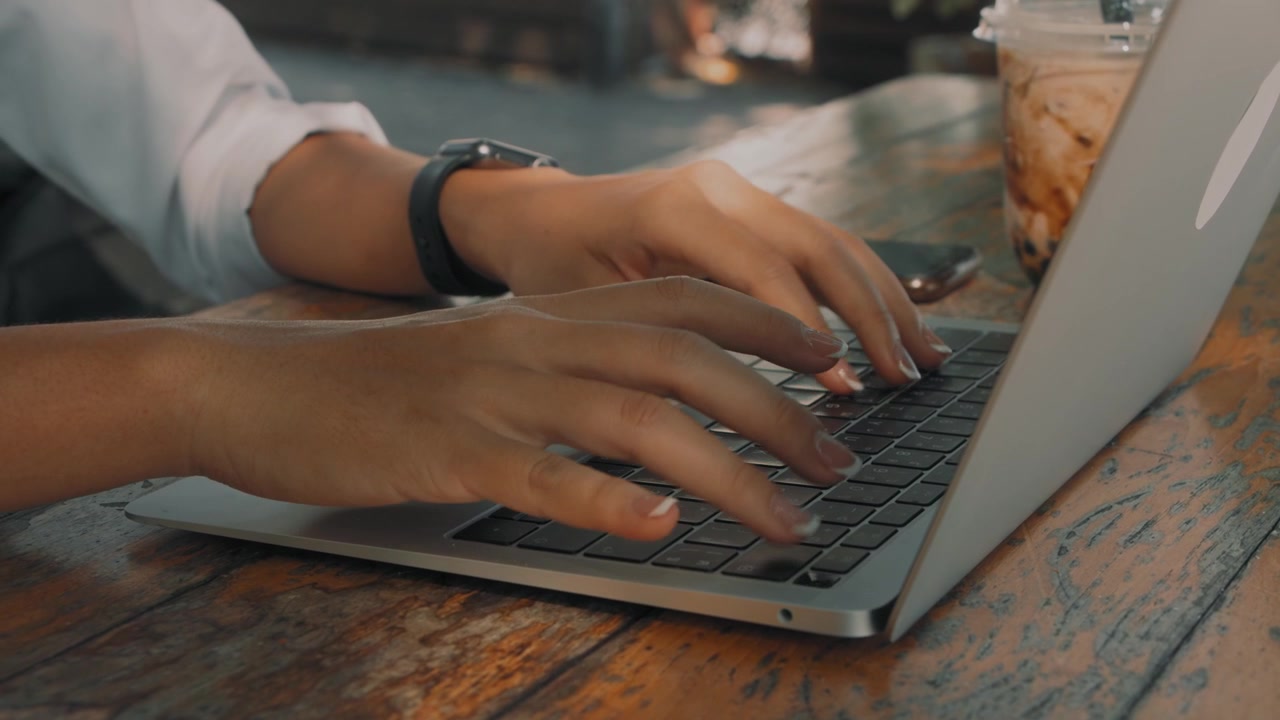 Persoon typt op laptop aan houten tafel in café