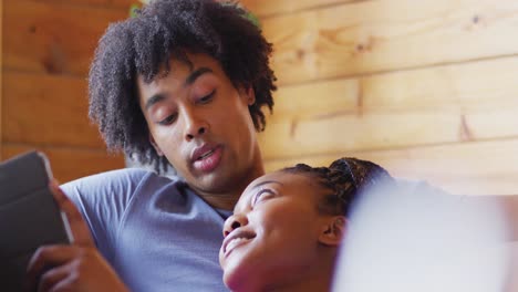 Happy-african-american-couple-using-tablet,-sitting-on-sofa-in-log-cabin,-slow-motion