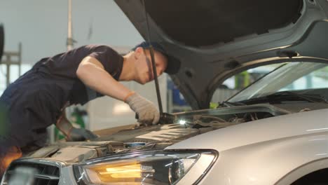 auto mechanic examining engine at car hood in auto repair workshop with light in the hand. repairman checking for customer to safety maintenance support before long trip. business and transportation c