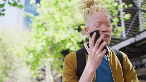 happy albino african american man with dreadlocks in park talking on smartphone