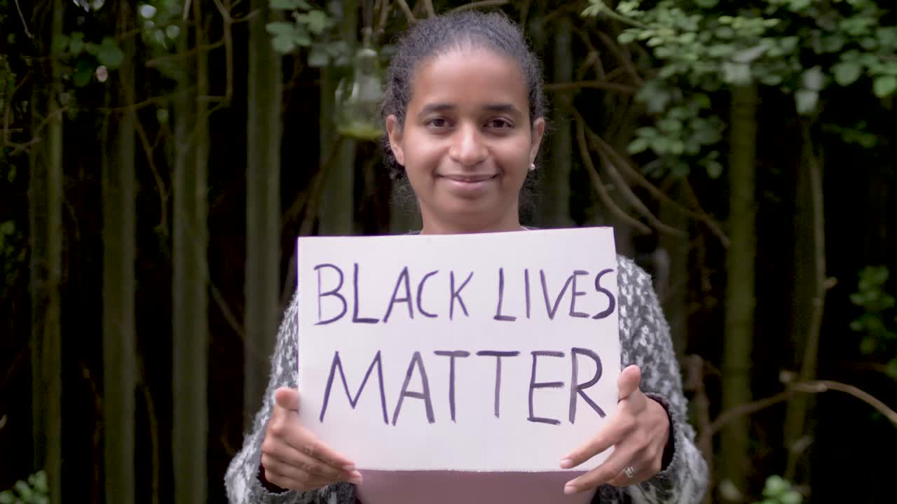 Attractive Black Woman holds &amp;quot;Black Lives Matter&amp;quot; Poster in front of her Face and smiles friendly