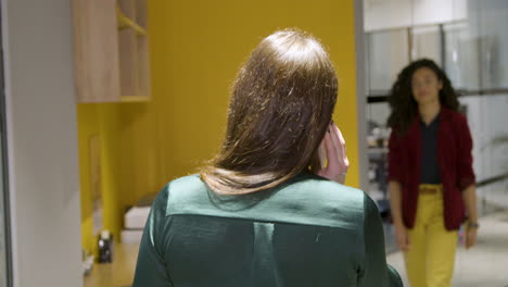 Rear-View-Businesswoman-Talking-On-Smartphone-In-Corridor