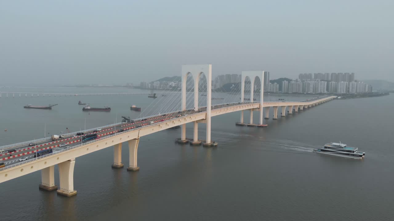 Aerial backwards reveal shot of ferry sailing away Sai Van Bridge in Macau with Taipa skyline as backdrop