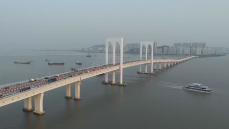 aerial backwards reveal shot of ferry sailing away sai van bridge in macau with taipa skyline as backdrop