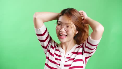 안경을 쓰고 웃고 녹색 화면을 통해 머리를 가지고 노는 행복한 장난기 많은 아시아 소녀