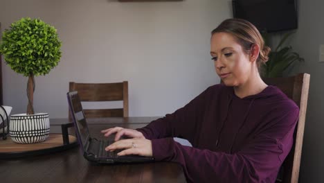 mujer seria escribiendo en su laptop trabajando en casa