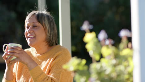 happy senior biracial woman drinking coffee on terrace, slow motion, copy space