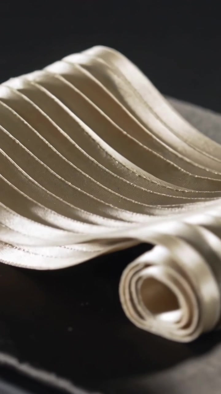 Vertical video: Uncoiling pleated strip loosening, smoothing across dark surface showing stitching