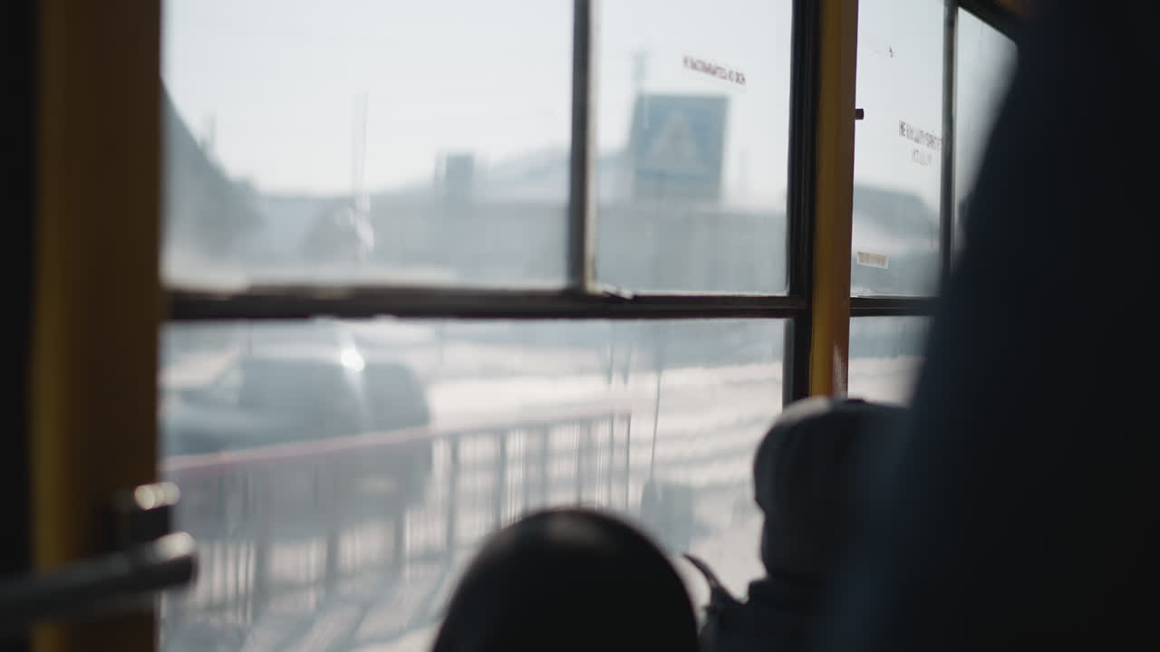 Window view from moving tram shows blue stop sign sliding past while passengers sit under winter light, blurred glass and frames, snow bright outside, urban transit with gentle motion along route