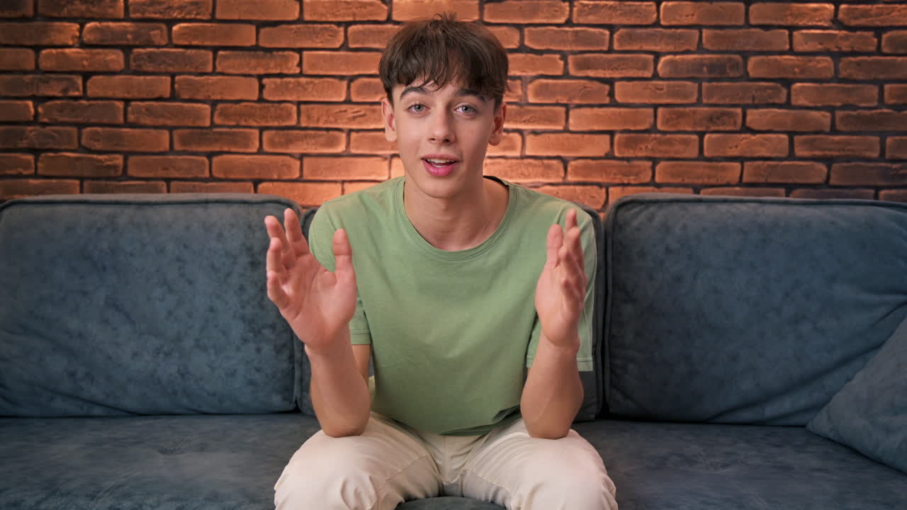 Un giovane blogger influencer seduto su un divano che parla e guarda nella fotocamera