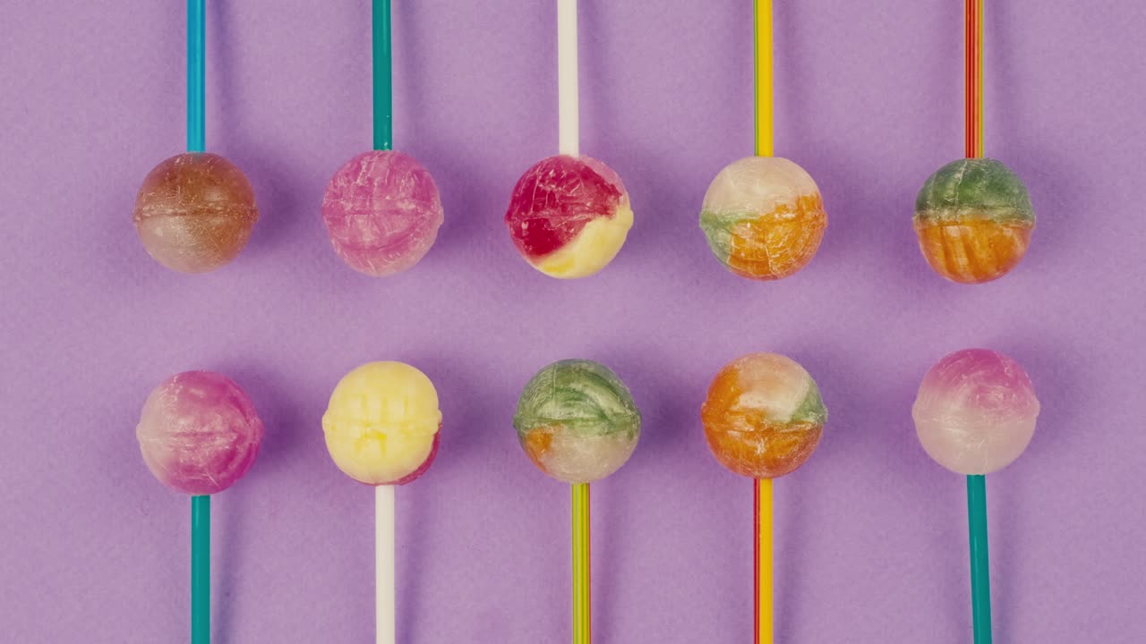 Sweet lollipops on color purple background. Bright texture sugar candies close up top view. Composition of favorite children's summer sweets. Studio shot for shop, supermarket, confectionery