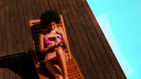 Gorgeous-woman-in-pink-bikini-drinking-cocktail-by-swimming-pool