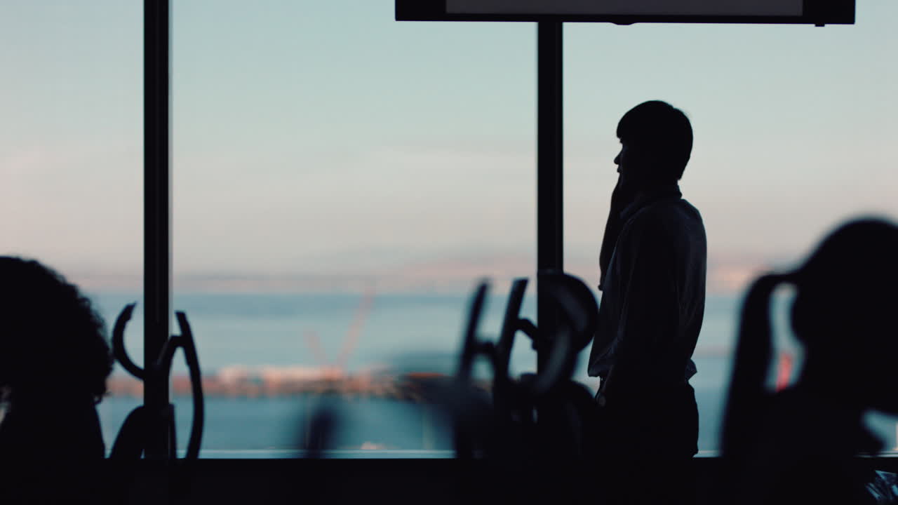 스마트폰을 사용하는 사업가의 실루 ⁇  휴대폰으로 통화하고 휴대폰으로 채팅하고 창문 밖을 바라보는 기업 경영자가 바쁜 사무실에서 늦게 판매를 논의하고 있습니다.