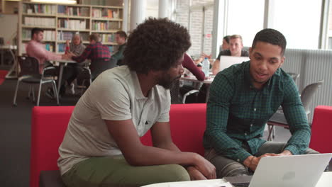 male university student working in library with tutor