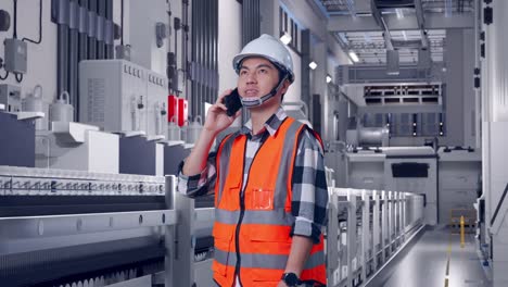 side view of asian male engineer with safety helmet talking on smartphone while standing at pharmaceutical factory, vaccine production facility