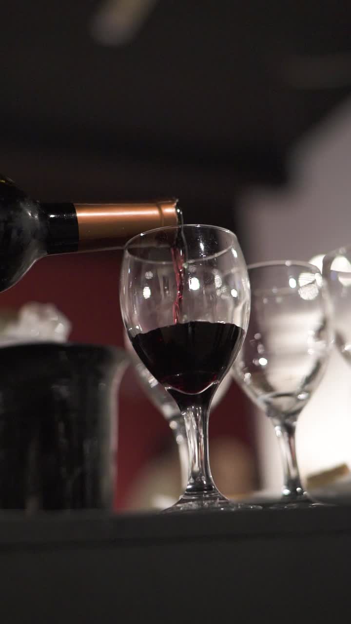 Primo piano al rallentatore di una bottiglia che versa vino rosso in un calice di cristallo durante una cena di lavoro.