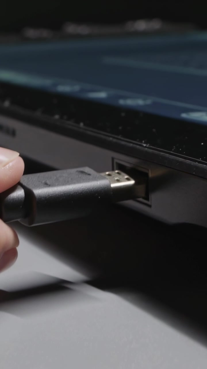 Vertical video: Camera focusing causing hand inserting USB plug into laptop port at desk to connect