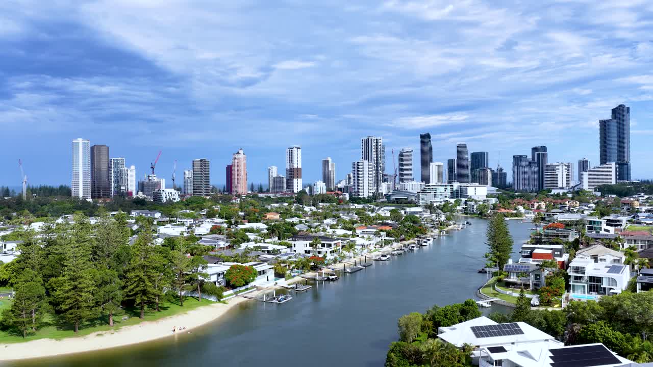 Drone glides above canal, revealing upscale homes, private docks, pools, and city skyline