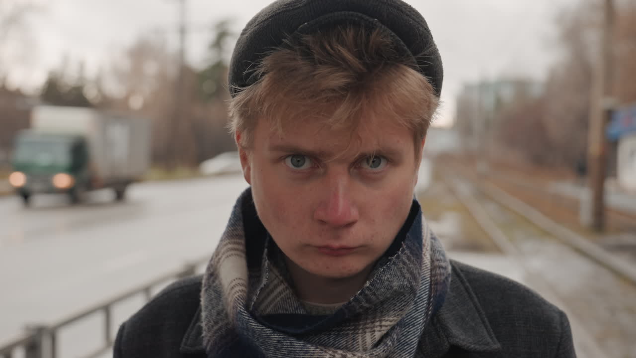 White creator with brooding downward gaze, damp platform and passing truck in background, knit cap and muted scarf, intense stare builds tension, cinematic indie tone with raw emotion