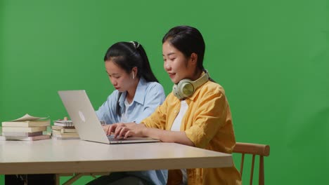 asian woman students writing and typing on a laptop while sitting on a table in the green screen background classroom