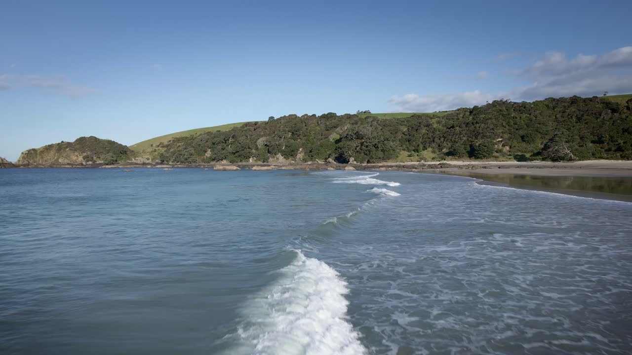 olas rompiendo hacia la playa de arena blanca del parque regional tawharanui - toma aérea