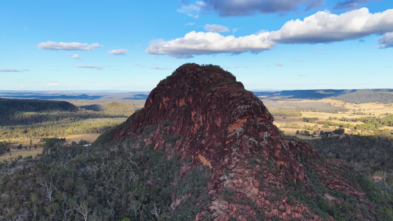 Drone glides over volcanic outcrop, revealing rugged sandstone peak and expansive Australian landscape