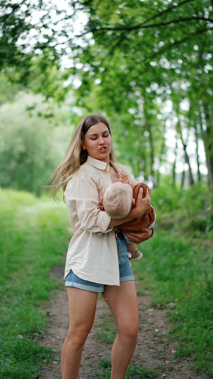 Happy mother waving her baby boy in hands standing in the nature. Mom and son spend time together outdoors in summer. Vertical video.