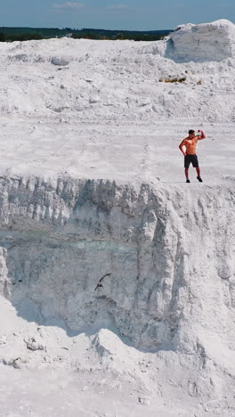 muscular sportsman on a white hill. view from above on a strong guy who is showing his strength on the natural background. bodybuilder on a rocky canyon. aerial view. vertical video