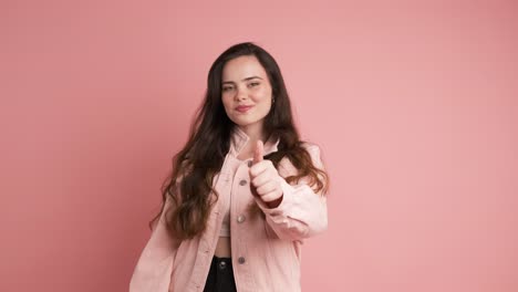 happy young woman showing thumbs up in pink studio